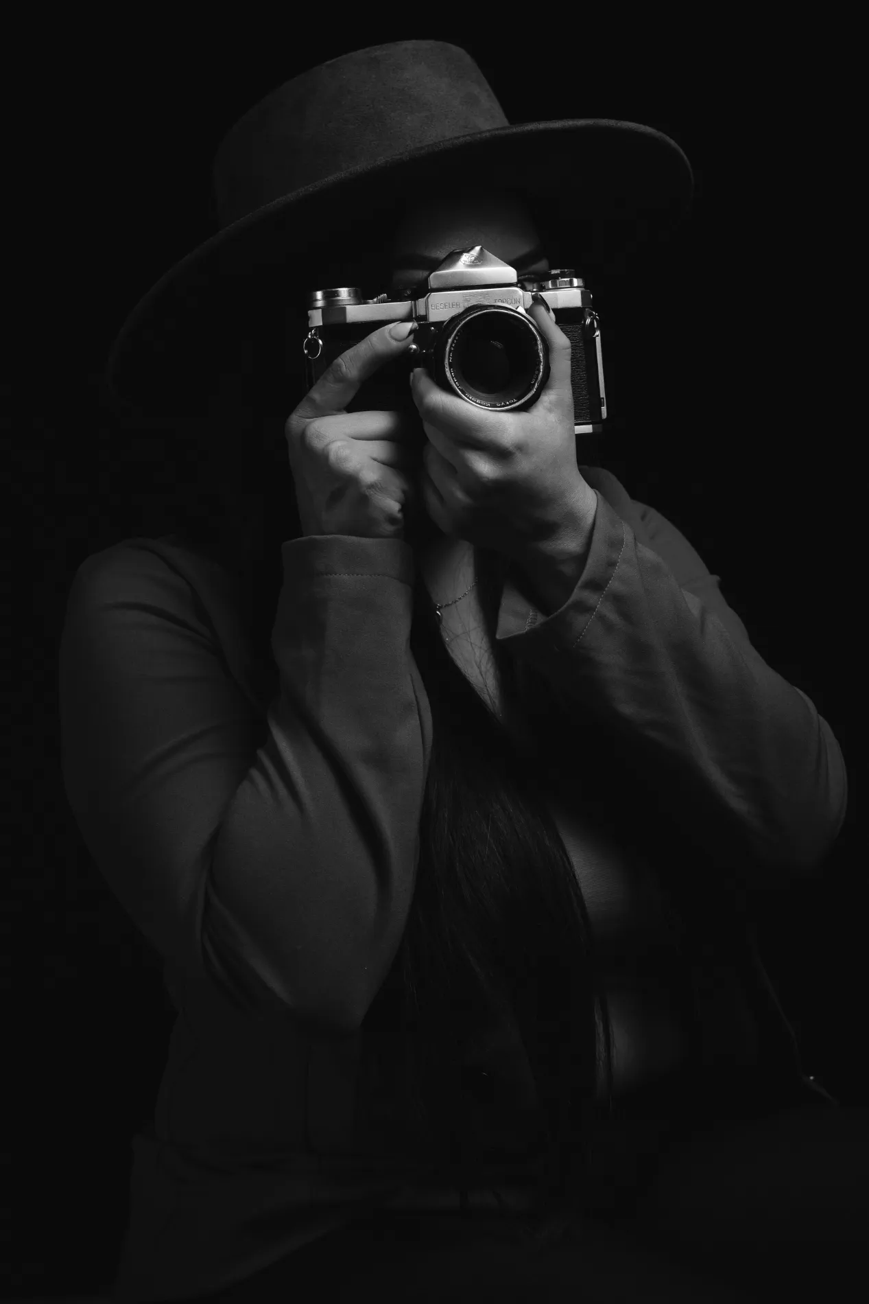 Alma Vera en blanco y negro, con sombrero y su cámara de película frente a la cara